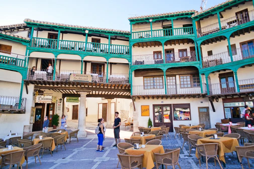 Terrazas de café bajo los balcones corridos de madera verde de la Plaza Mayor de Chinchón, en una excursión privada con chófer desde Madrid